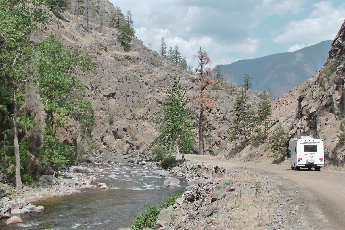 A gravel backcountry road beside a rocky creek in a dry, steep-sided valley.