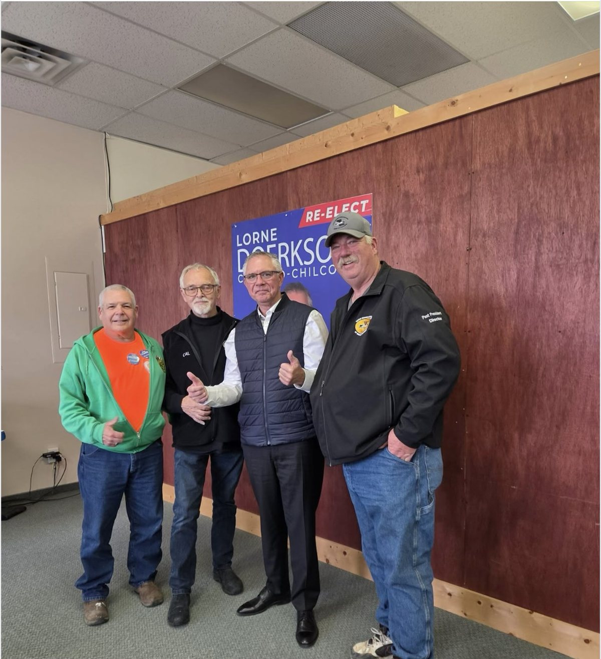 Lorne Doerkson, in a vest, gives a thumbs-up beside three officers of the Quad Riders ATV Association in front of a blue banner reading Re-elect Lorne Doerkson, Cariboo-Chilcotin.