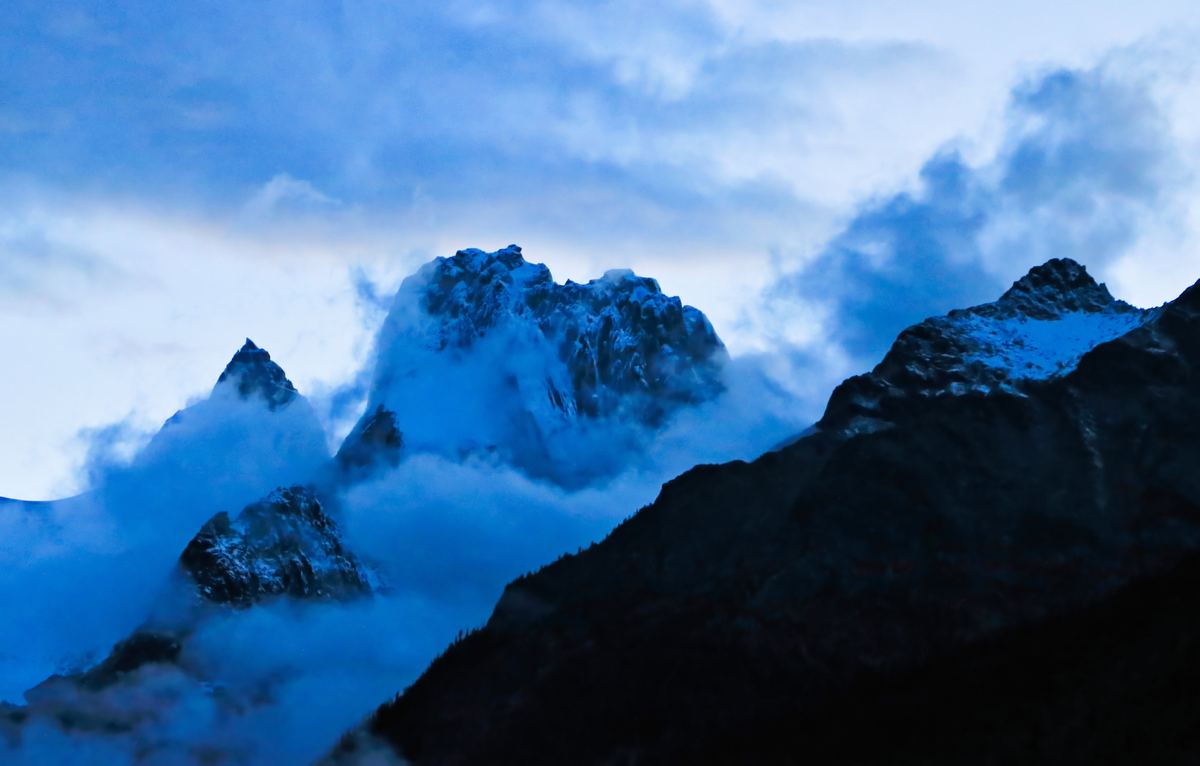 Granite spires of the Bugaboo Range rising out of blue cloud and mist at dusk.
