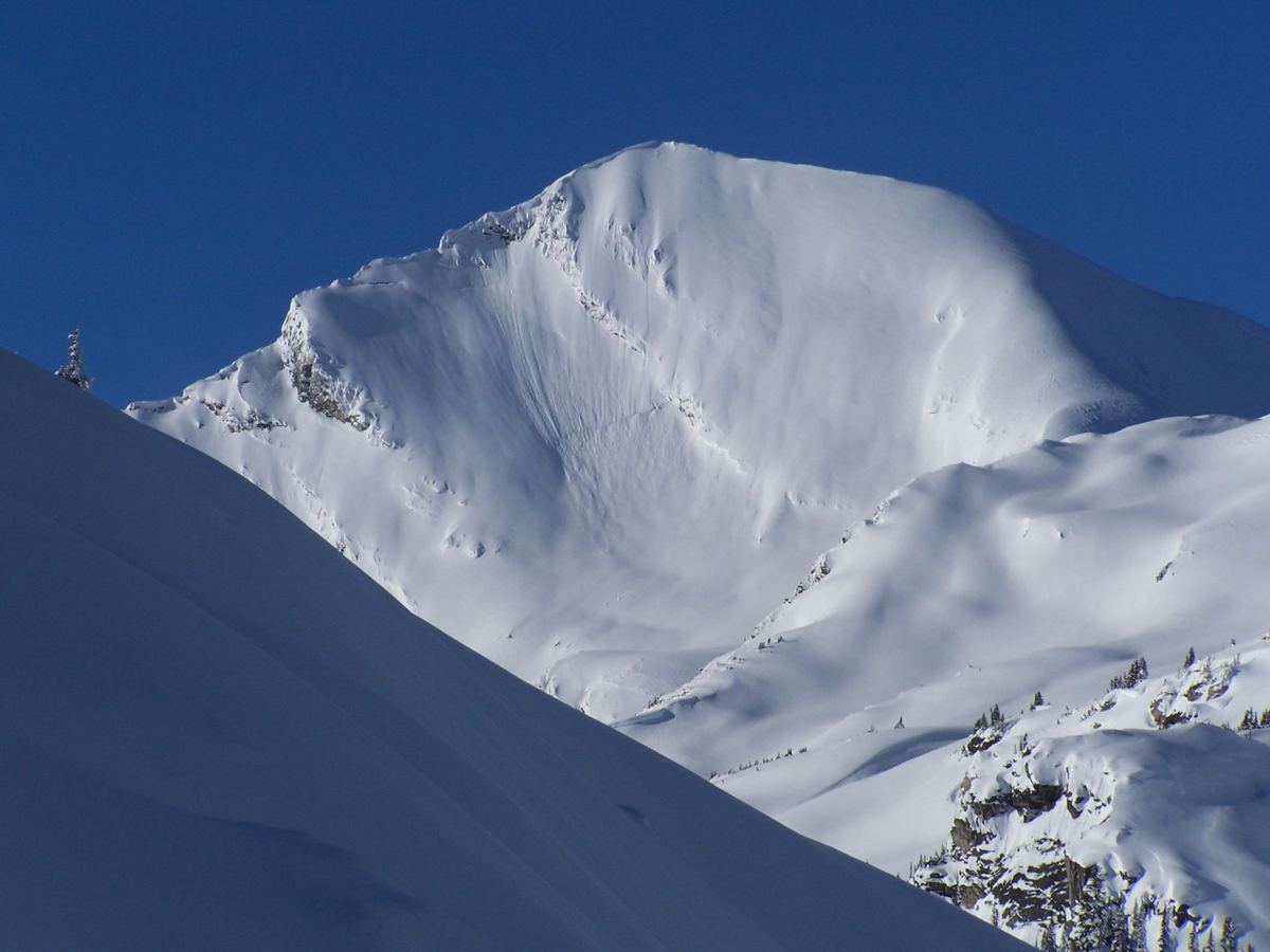 The snow-covered east face of Catamount Peak in winter, with tracks across the slope below.