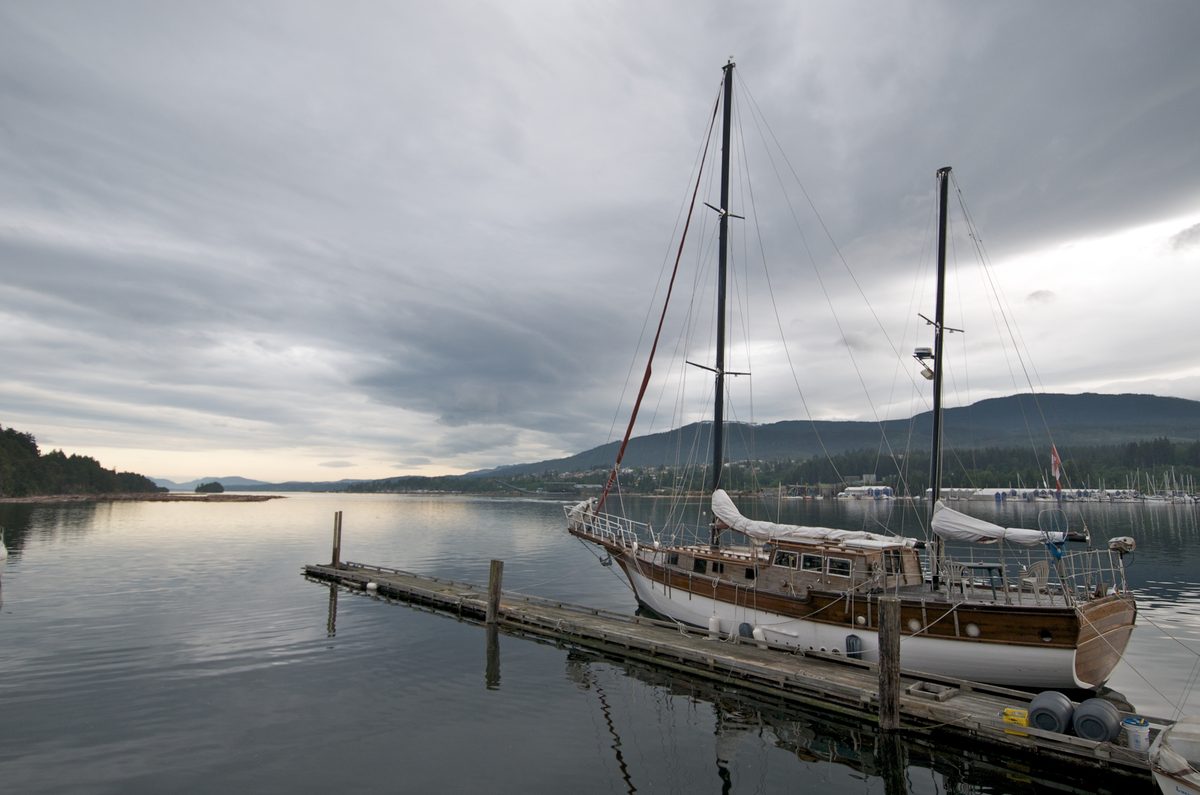 A wooden ketch tied to a long dock in Ladysmith Harbour under a grey evening sky.