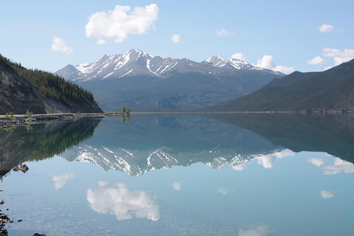 Snowy peaks reflected in the still water of Muncho Lake along the Alaska Highway.