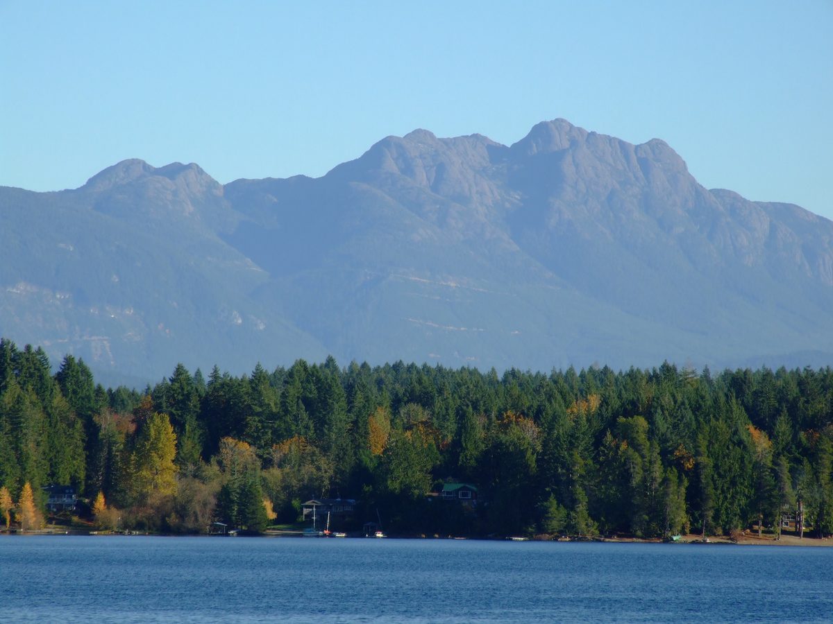 Mount Arrowsmith rising above a forested shoreline across the still water of Sproat Lake.