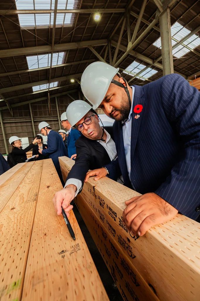 Ravi Parmar in a white hard hat and suit, leaning over a large timber beam at a manufacturing plant.