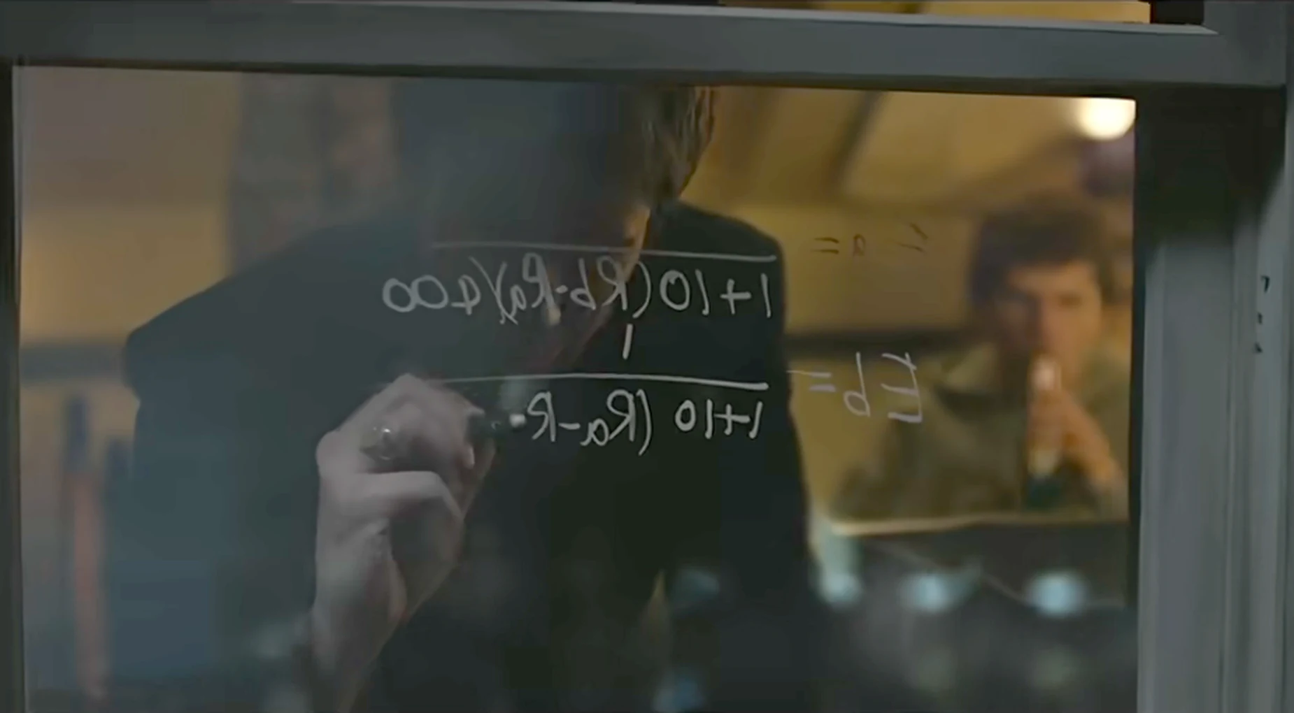 A hand writes a probability equation in marker on the inside of a window at night, the letters reversed from the viewer&rsquo;s side; a second man sits at a desk in the lit room beyond the glass.