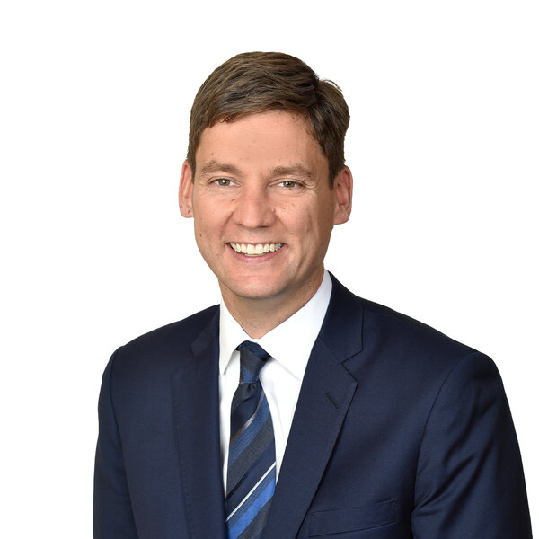 David Eby, Premier of British Columbia and leader of the BC NDP: a campaign headshot on a white background, in a navy suit and striped tie.