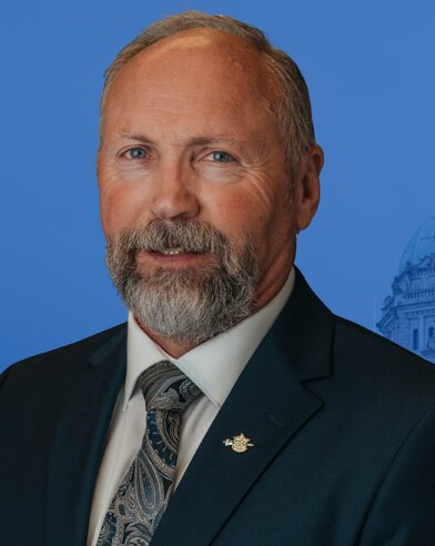 Ward Stamer, Conservative candidate for Kamloops-North Thompson: a campaign headshot against a blue ground with the legislature dome behind him.