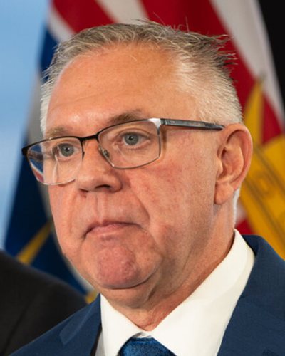 Lorne Doerkson at a lectern in a blue suit, with the B.C. flag behind him.