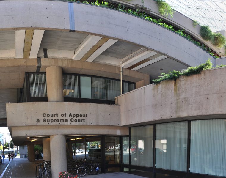 The concrete entrance of the Vancouver Law Courts, with the words Court of Appeal and Supreme Court on a curved wall above glass doors and parked bicycles.