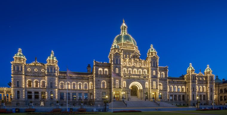 The B.C. Parliament Buildings at dusk, outlined in thousands of white lights under a deep blue sky.