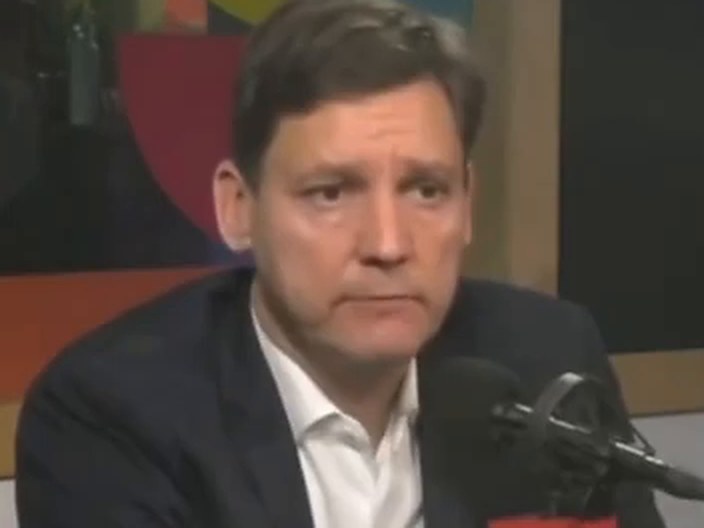 David Eby listening, his mouth set, behind a CBC microphone.