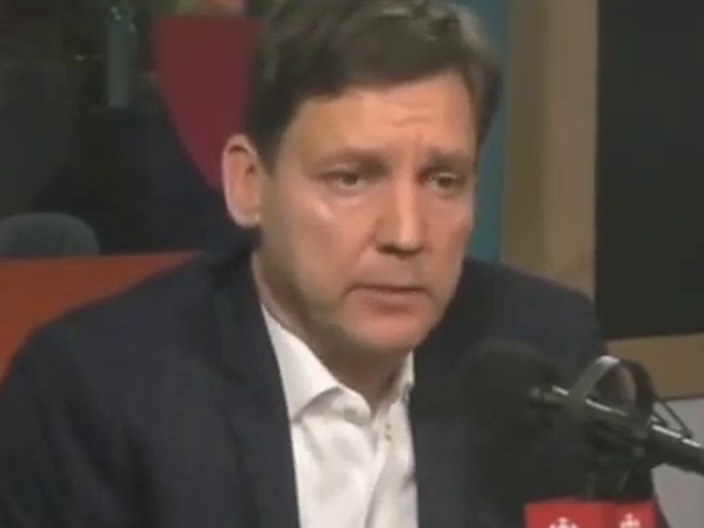 David Eby, looking down, speaking at a CBC microphone.