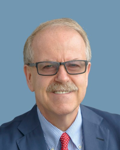 Jock Finlayson, smiling, in a blue blazer, striped shirt and red tie.