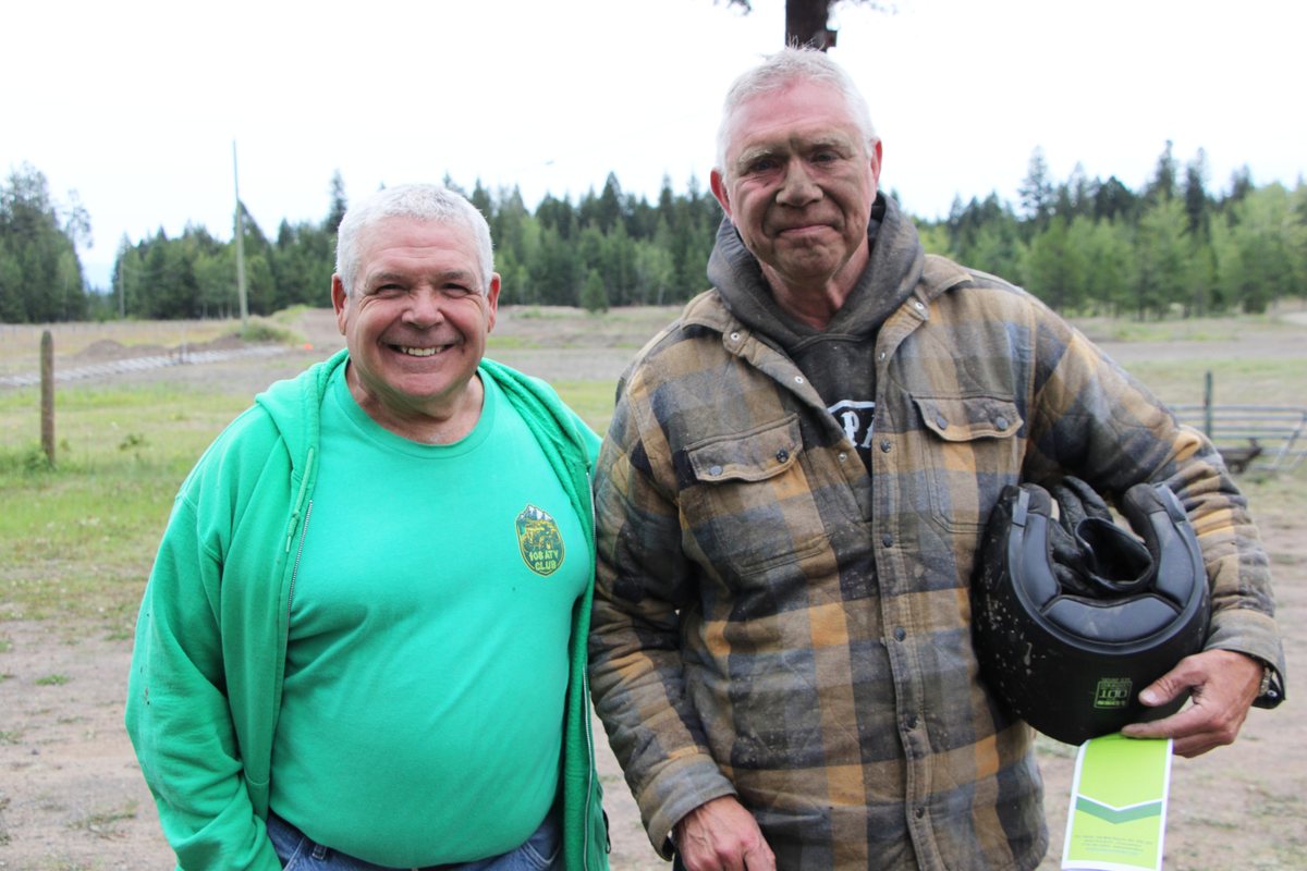 Mark Redl, smiling in a green 108 ATV Club shirt, beside Lorne Doerkson, whose face is spattered with mud and who holds a riding helmet.