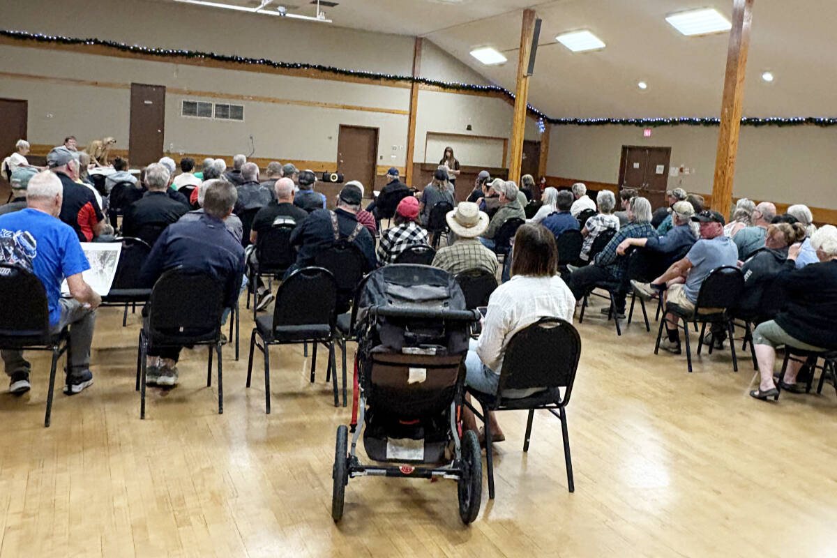 Rows of people seated in a community hall, seen from the back, at a public meeting.