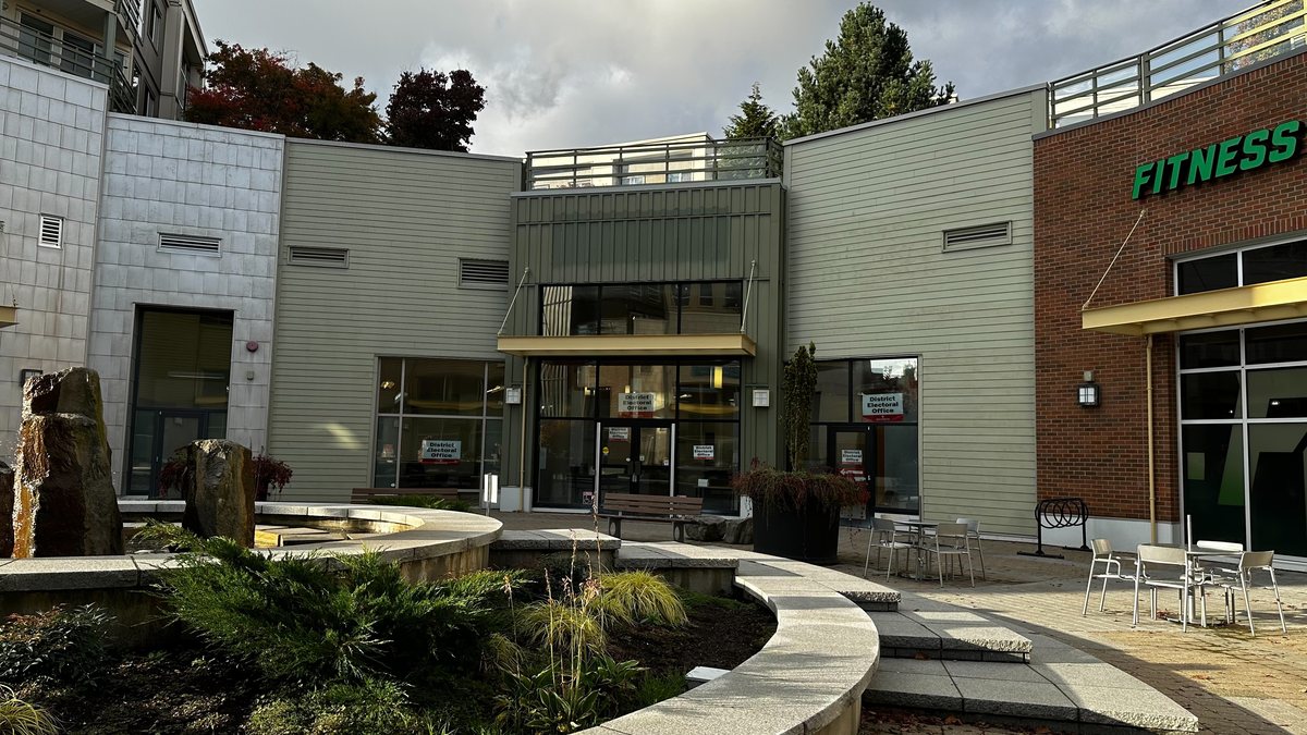 The entrance of a district electoral office in a Surrey shopping plaza, with Elections BC signs on the glass doors, under an autumn sky.