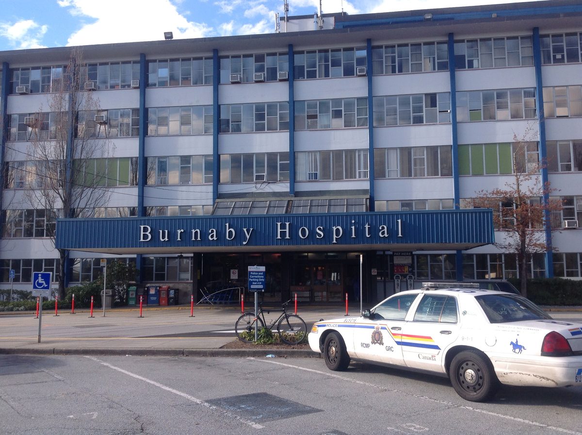 The older Burnaby Hospital building, with blue window frames and a long entrance canopy, and an RCMP cruiser parked out front.