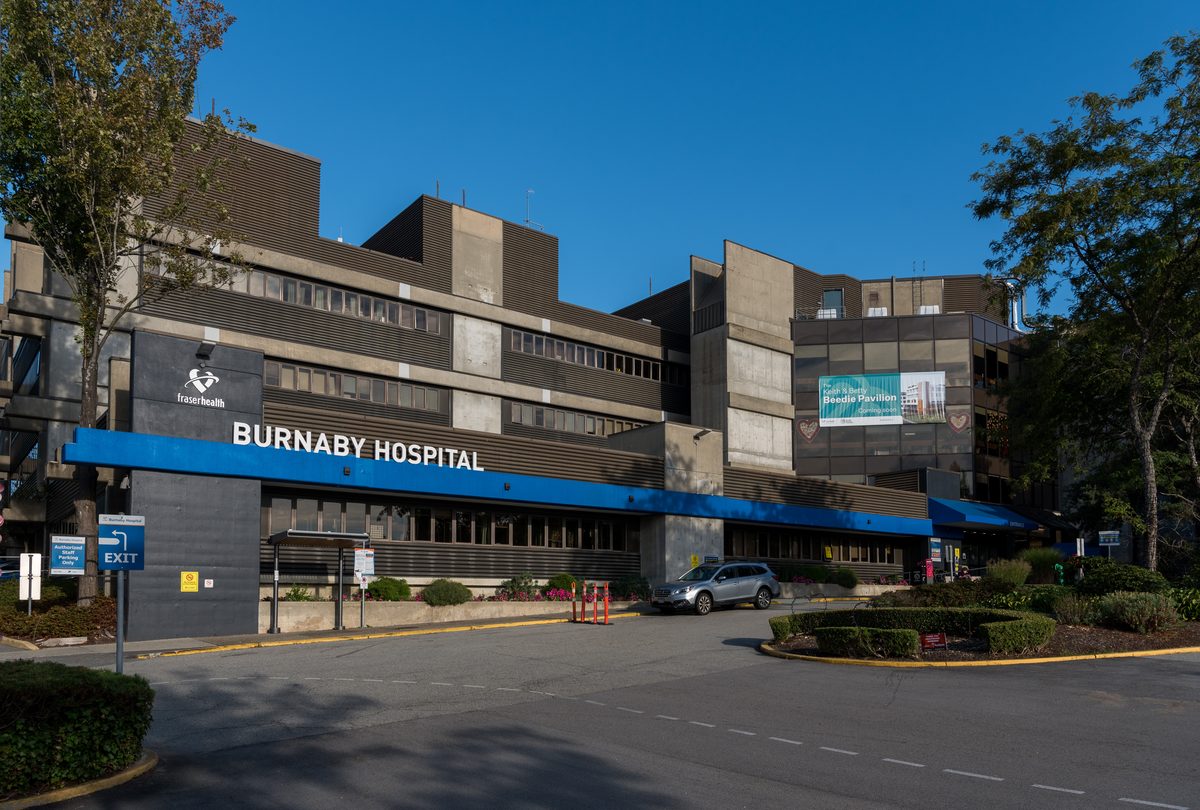 The front entrance of Burnaby Hospital under a blue sky, with its blue canopy and the Fraser Health sign.
