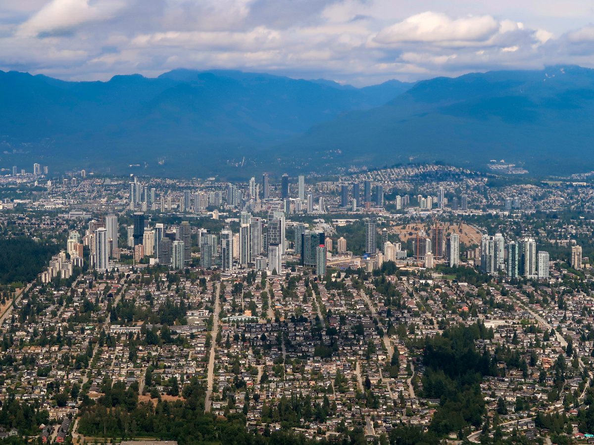 An aerial view of Burnaby, with the towers of Metrotown rising from streets of houses and the North Shore mountains behind.