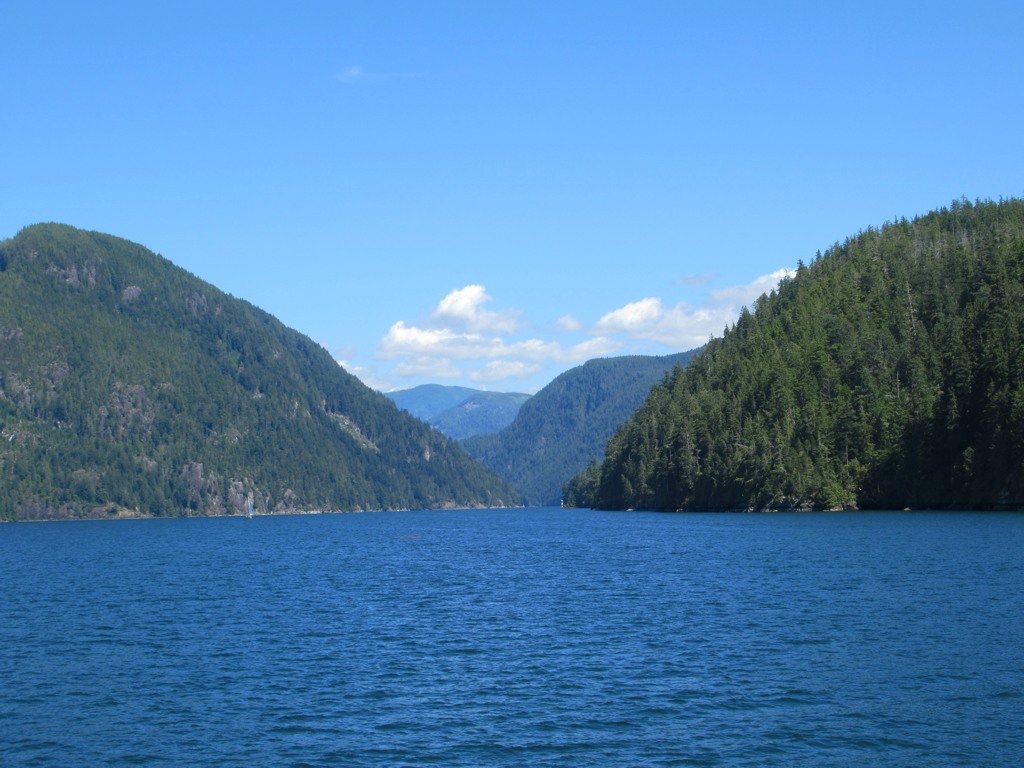 The Alberni Inlet running between steep, forested hillsides under a blue sky.